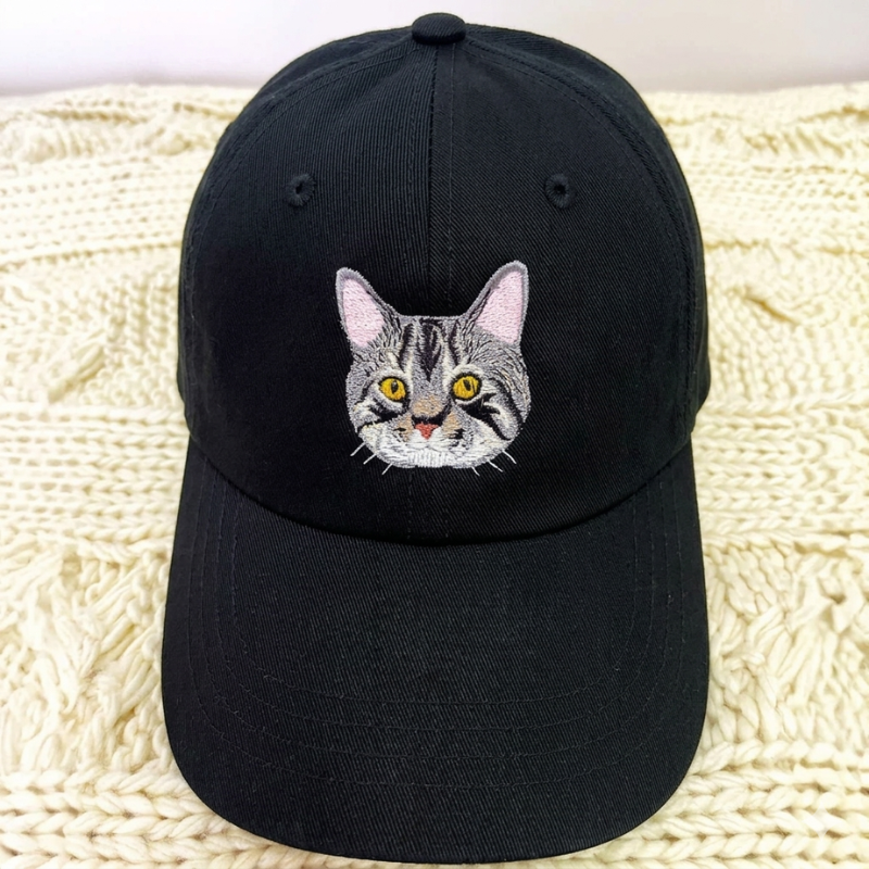 Črna kapa z vezenim realističnim portretom sive mačke.