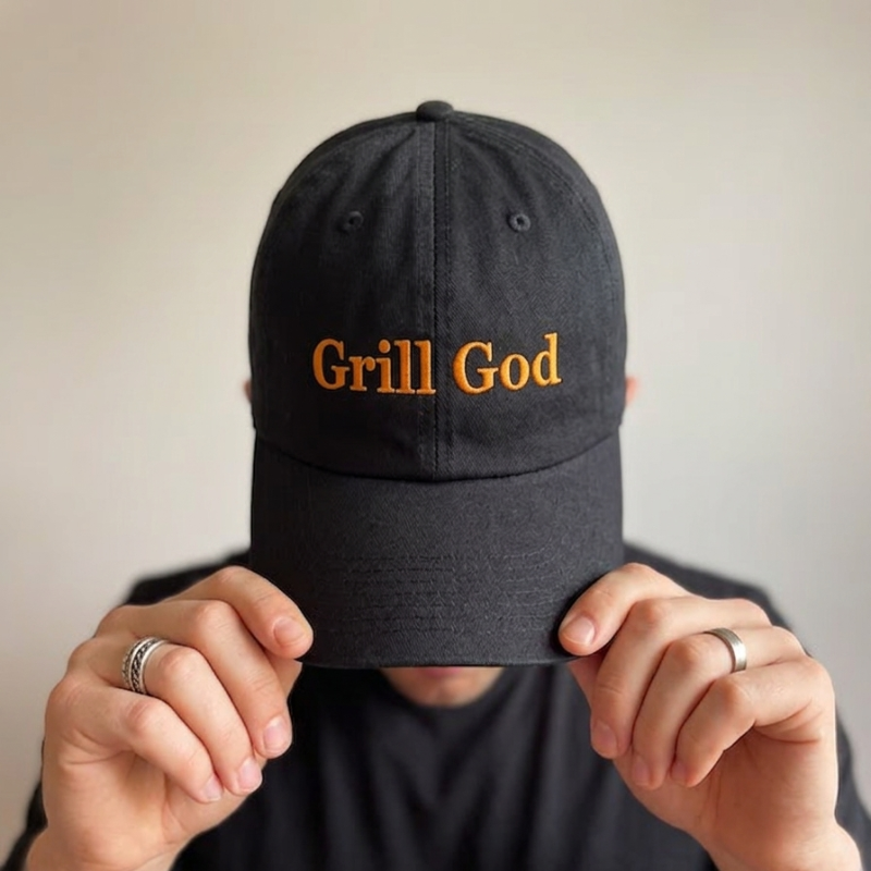 Črna personalizirana kapa z oranžnim vezenim napisom "Grill God" – idealno darilo za moške in ljubitelje peke na žaru