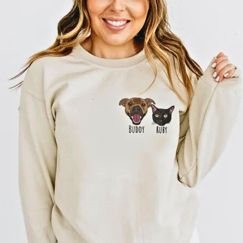 Ženska v bež majici z dolgimi rokavi, ki prikazuje vezenje dveh ljubljenčkov na prsnem delu.