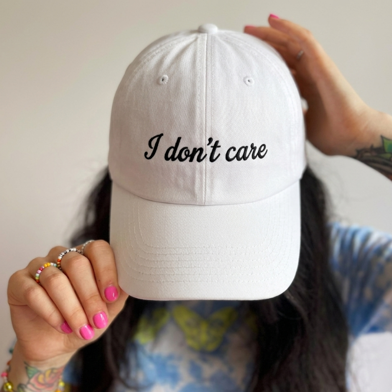 Bela personalizirana kapa s šiltom s črnim napisom "I don't care" – minimalistično vezenje po želji.